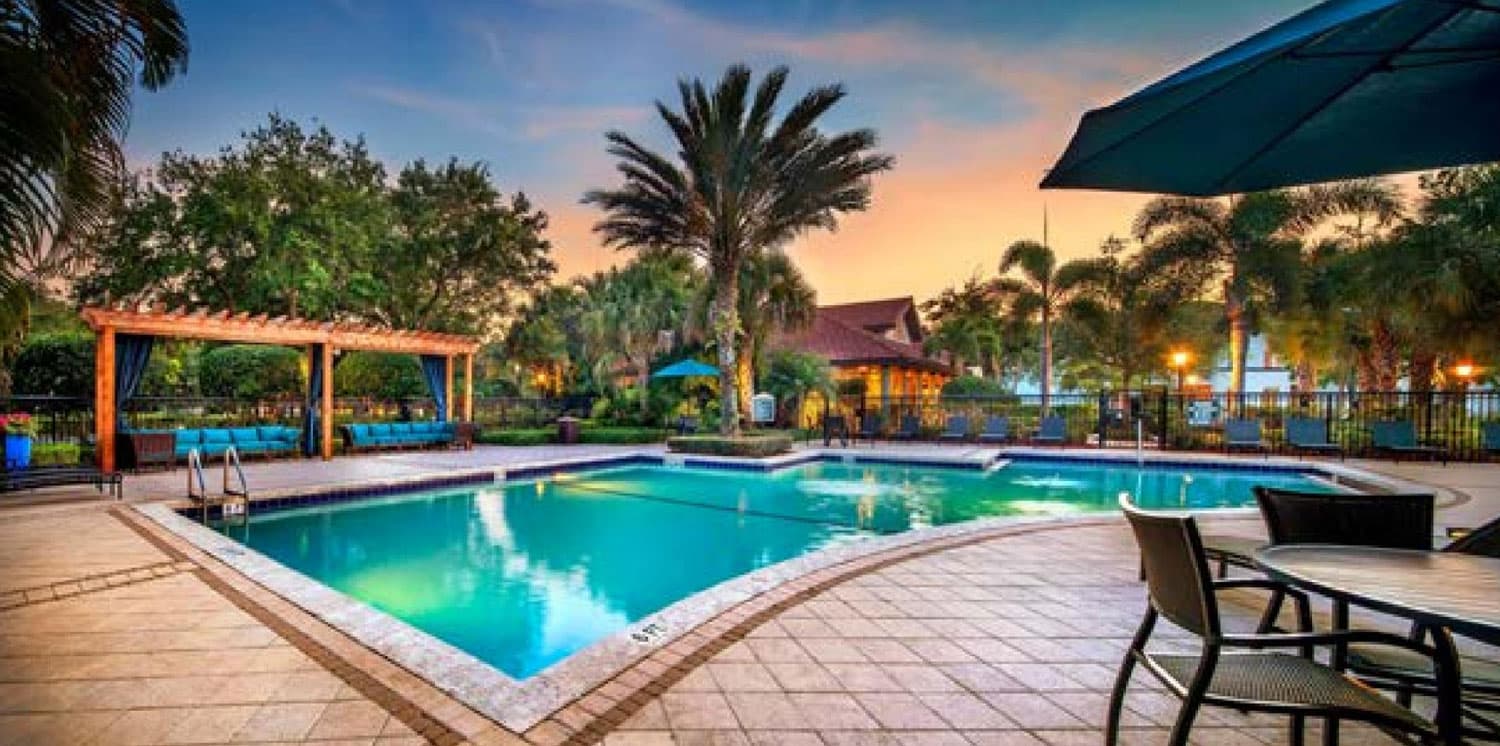 A stylish swimming pool surrounded by palm trees and buildings with red tile roofs.