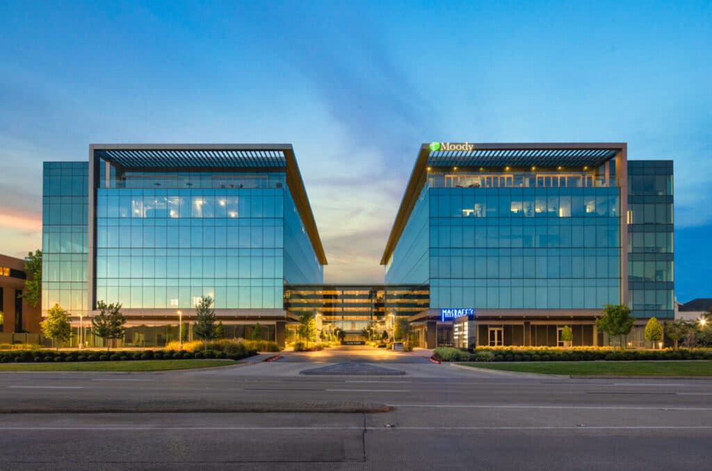 Photo of a large building with many windows, with a brand Moody at the top right side. The building has twin units facing each other, connected by a lobby structure in the middle.