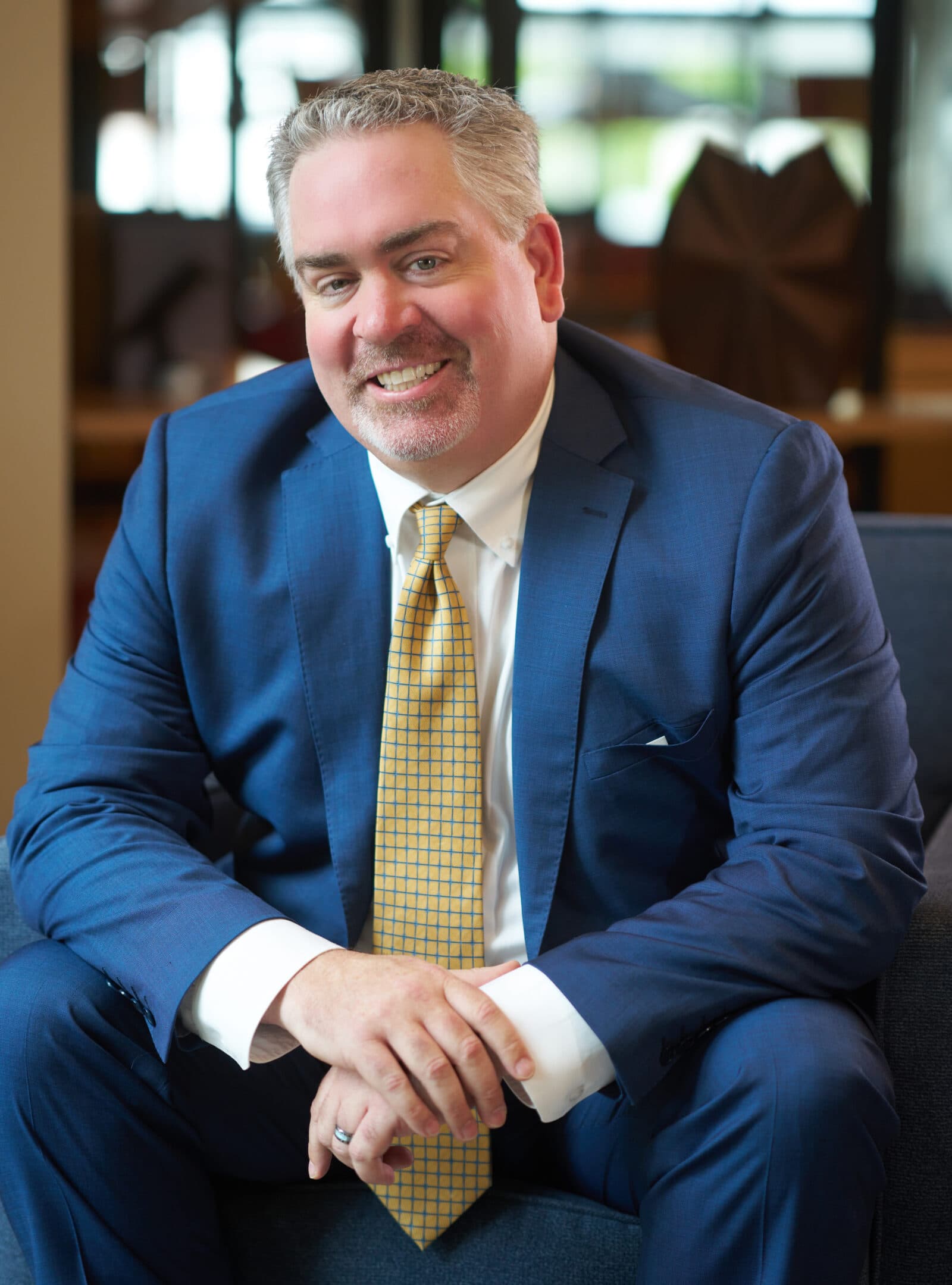 James is a friendly white man smiling at the camera. He's wearing a blue suit, matching pants, white shirt, and yellow checkered tie.