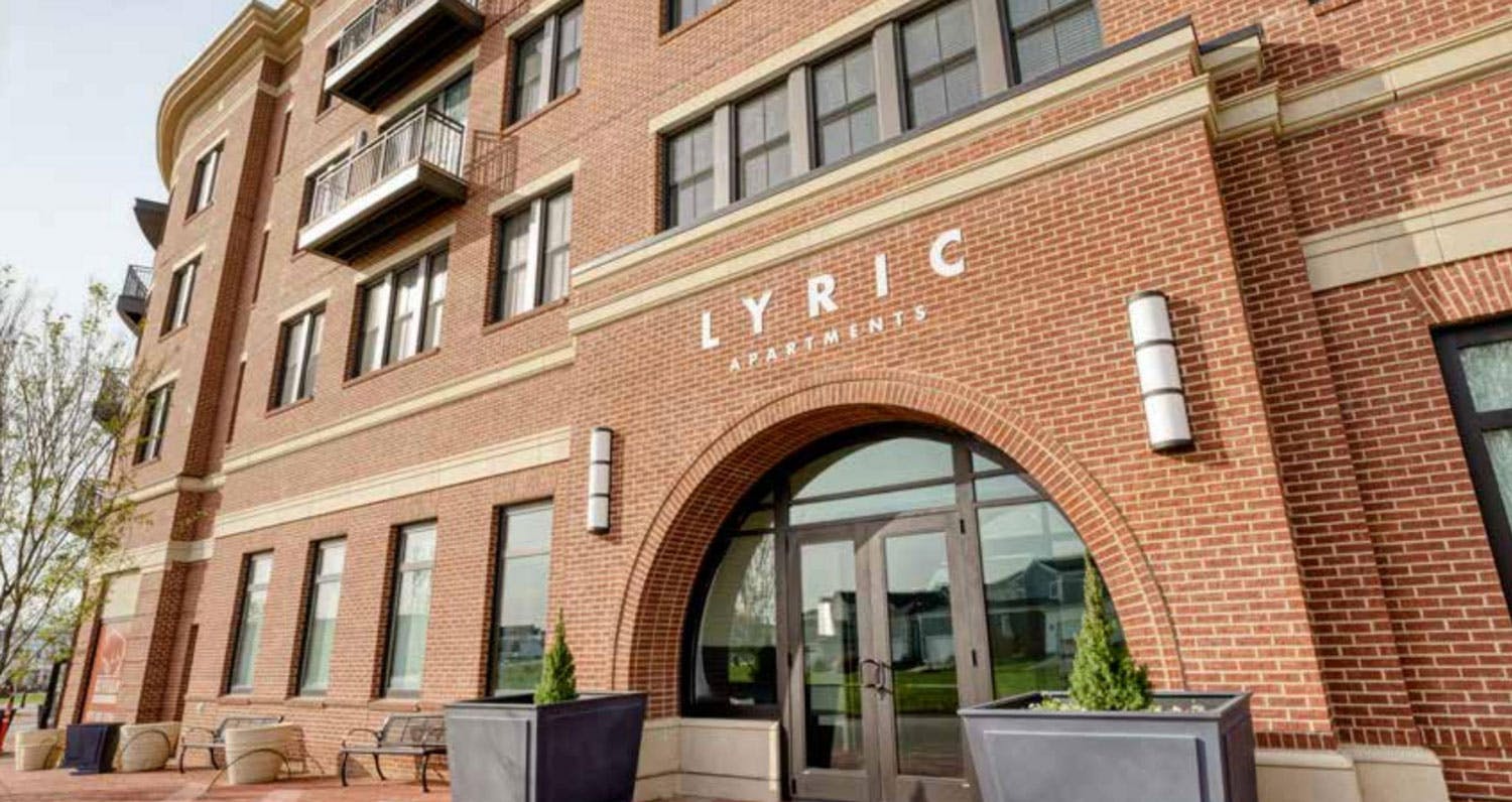A large 4 story red brick building with the words Lyric Apartments above the arched entrance. There are many windows and a few balconies.