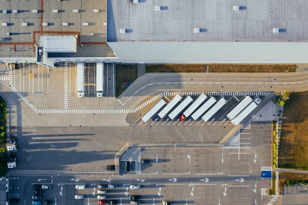 Bird's eye view of an industrial building with a parking lot full of freighter trucks and their tractors.